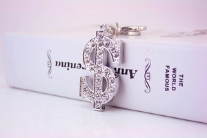 Close-up of a silver dollar sign keychain with sparkling rhinestones on a white book
