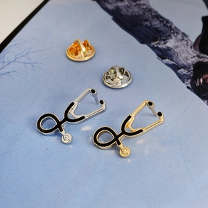 Detail of stethoscope brooches in gold and silver finish with black enamel and butterfly clasp