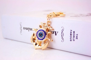 Macro shot of gold anchor and helm keychain featuring a blue rhinestone evil eye charm
