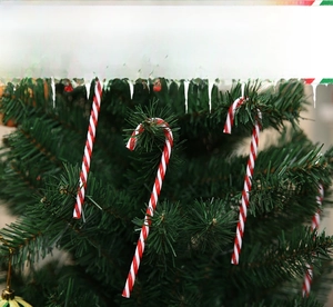 Close-up of red and white striped candy cane ornament hanging on a lush Christmas tree branch