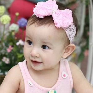 Detail of pink lace baby headband with satin roses and pearls worn by infant