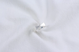 Close-up of a silver 925 minimalist brushed ribbon bow ring on white linen fabric