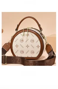 Close-up of beige round crossbody bag with brown trim and woven fashion strap