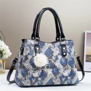 Close-up of snakeskin print tote bag with black patent leather trim and plush pom pom