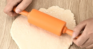 Detailed view of hands using a 30.5cm orange silicone rolling pin on a wooden table