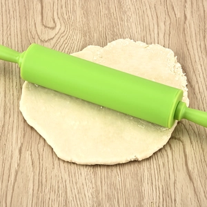 Green silicone rolling pin with ergonomic handles rolling dough on a wooden surface