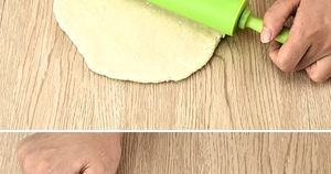 Close-up of green non-stick silicone rolling pin flattening dough on wooden table