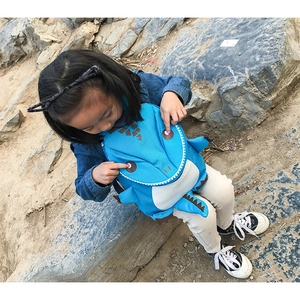 Blue cartoon dinosaur backpack with 3D fins shown in a natural outdoor park setting
