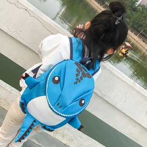 Outdoor shot of a child wearing a bright blue 3D dinosaur backpack with tail and fins
