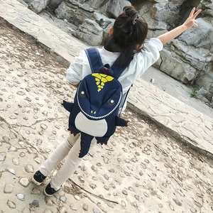Rear view of a blue cartoon dinosaur backpack worn by a toddler on a nature outing
