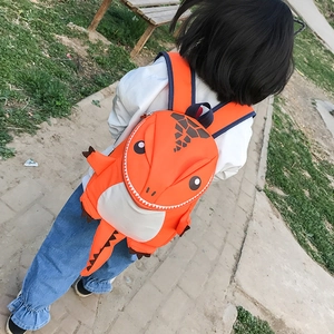 Rear view of child wearing an orange 3D dinosaur backpack with tail in a park setting