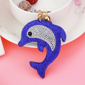 Macro shot of blue and white rhinestone dolphin keychain with gold metal clasp on pink background