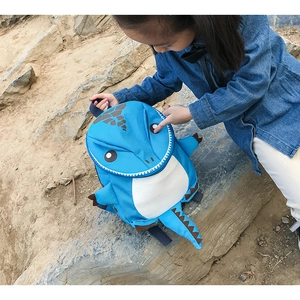Blue dinosaur backpack for kids shown with a child in an outdoor nature setting