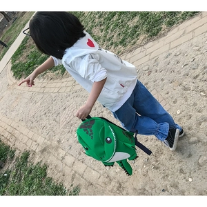 Detailed outdoor view of a green dinosaur backpack for kids with 3D fins and tail