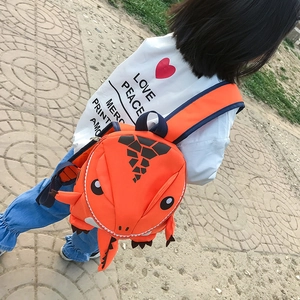Outdoor view of an orange cartoon dinosaur backpack with soft adjustable straps for kids