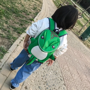 Outdoor view of children's green cartoon dinosaur backpack with soft brown spikes