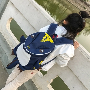 Detailed outdoor view of a navy blue dinosaur backpack with yellow spines for children