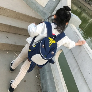 Detail view of a 3D dinosaur kid backpack with yellow spikes and wide straps in park