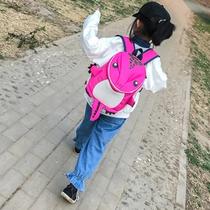 Rear view of a child carrying the pink cartoon dinosaur backpack with a 3D tail