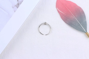 Detailed view of silver beaded open ring with round bead on minimalist feather backdrop