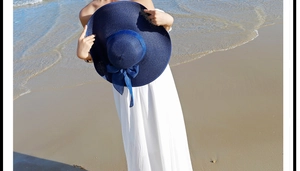 Detalle de un sombrero de paja azul marino con lazo sobre fondo de playa y las olas