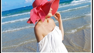 Detalle de sombrero de sol rosa fucsia con lazo frente a un fondo de playa real