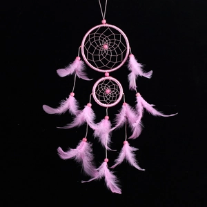 Atrapasueños rosa con dos aros y plumas colgantes sobre fondo negro de estudio