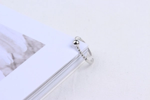 Close-up of minimalist silver beaded open ring displayed on an open magazine page