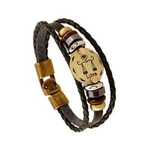 Macro detail of Libra zodiac bronze charm on multi-layer black braided leather bracelet