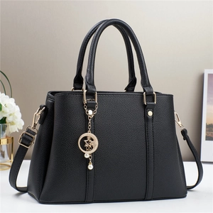 Black lychee leather tote bag with gold hardware and pearl charm on white table