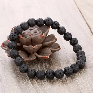 Natural porous black lava stone beaded bracelet on a rustic wooden surface with zen decor