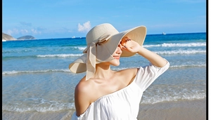 Detalle de un sombrero de paja beige de ala ancha con lazo, usado por una modelo en la playa