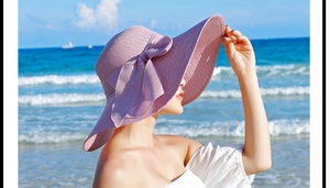 Detalle de un sombrero de paja lavanda con ala ancha y un gran lazo en una playa soleada