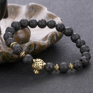 Lava rock beaded bracelet with gold leopard head charm on textured dark background