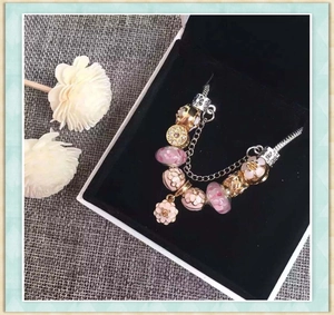 Pink and gold beads charm bracelet with floral enamel in a velvet lined jewelry box