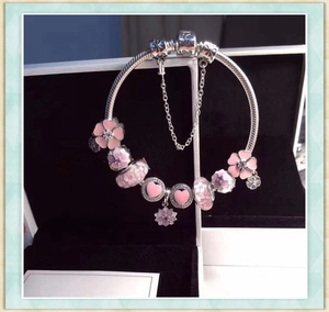 Close-up of silver charm bracelet with pink and white floral beads in a black gift box