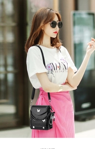 Detail showing small black crossbody bag with silver butterfly emblem and bear keychain charm
