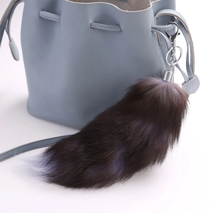 Macro detail of large fur fox tail keychain with silver metal clasp on a blue bag