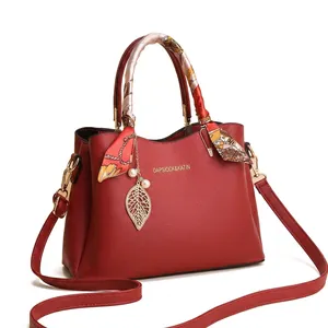 Vue détaillée du sac à main rouge en cuir litchi avec poignée en foulard et pendentif feuille