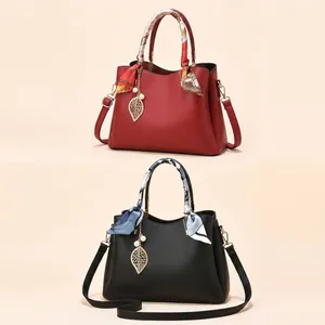 Gros plan du sac à main en cuir grainé rouge avec poignée foulard et breloque perle
