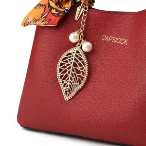 Détail d'un sac à main en cuir rouge avec pendentif feuille dorée et perles blanches