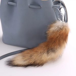 Detail of fluffy fox tail keychain in reddish-brown fur on a blue leather handbag