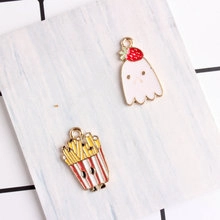 Detail of strawberry ghost and French fries enamel charms on white wood background