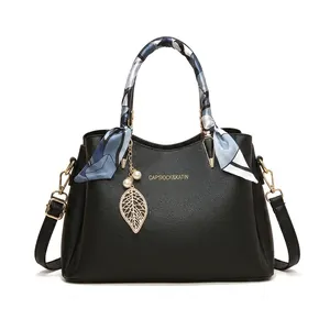 Détail du sac en cuir noir avec ferrures dorées et poignée ornée d'un foulard élégant