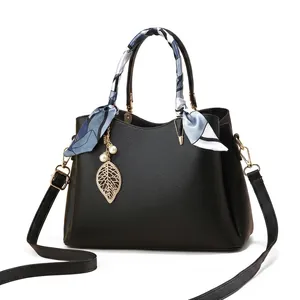 Détail du sac à main noir en cuir grainé avec breloque dorée et foulard en soie au manche