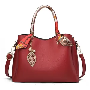 Détail du sac à main rouge en cuir grainé avec finitions dorées et foulard en soie