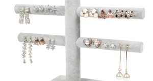 Detail view of pearl and rhinestone earrings displayed on a two-tier grey velvet stand