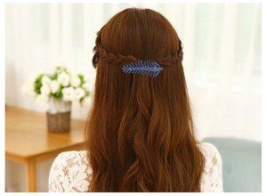 Blue feather-shaped hair clip with crystals shown on a model in a cozy indoor setting