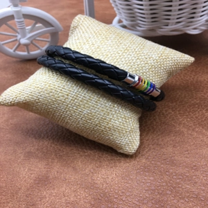 Detail of black braided leather bracelet with multi-color magnetic clasp on small pillow