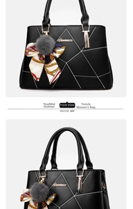 Detail view of black handbag featuring white geometric stitching and a gray fur pom pom